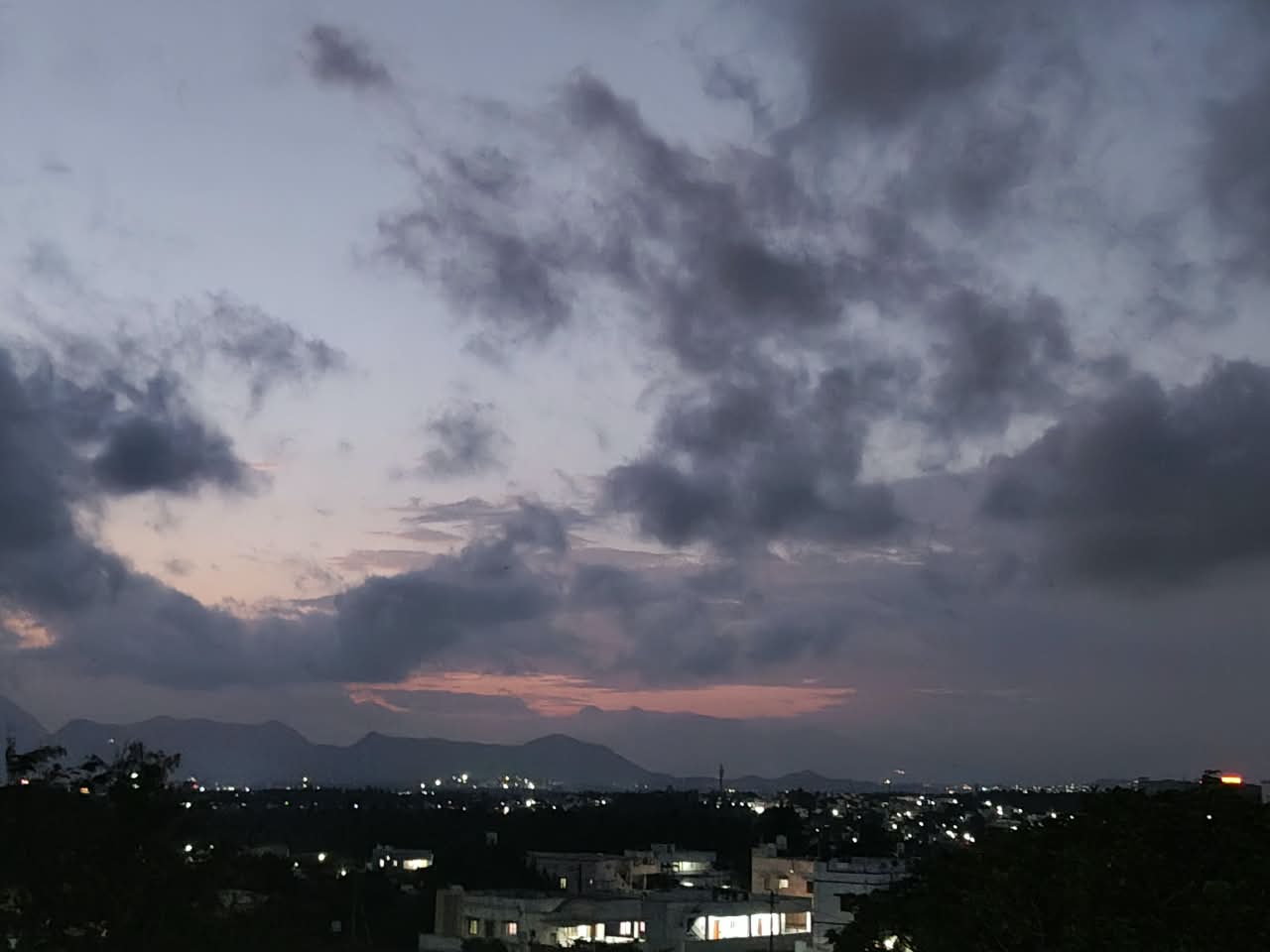 Dusk over the city, heavy clouds with a pink seam above the hills