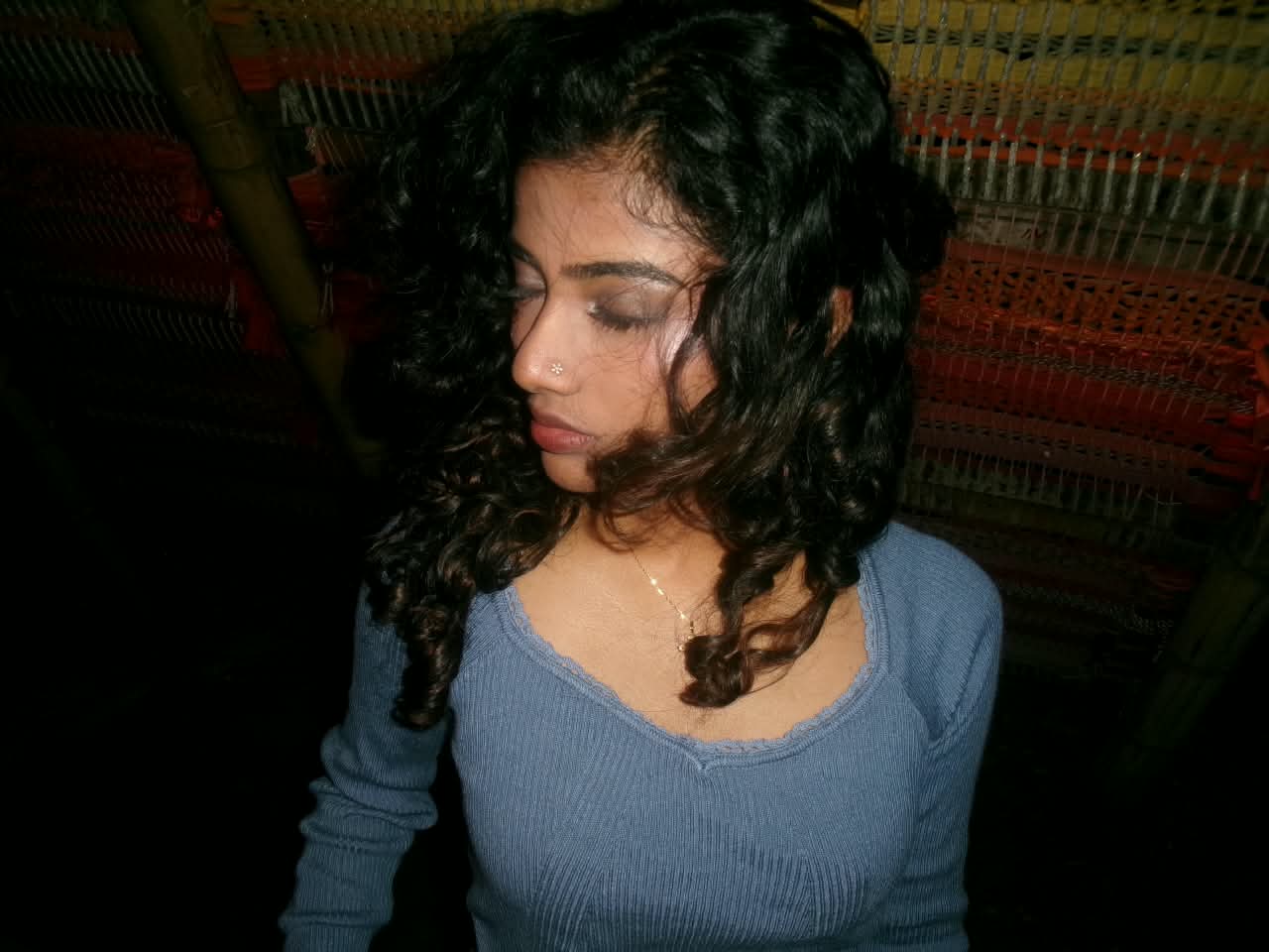 Portrait of a girl with curly hair, eyes closed, in front of a woven wall